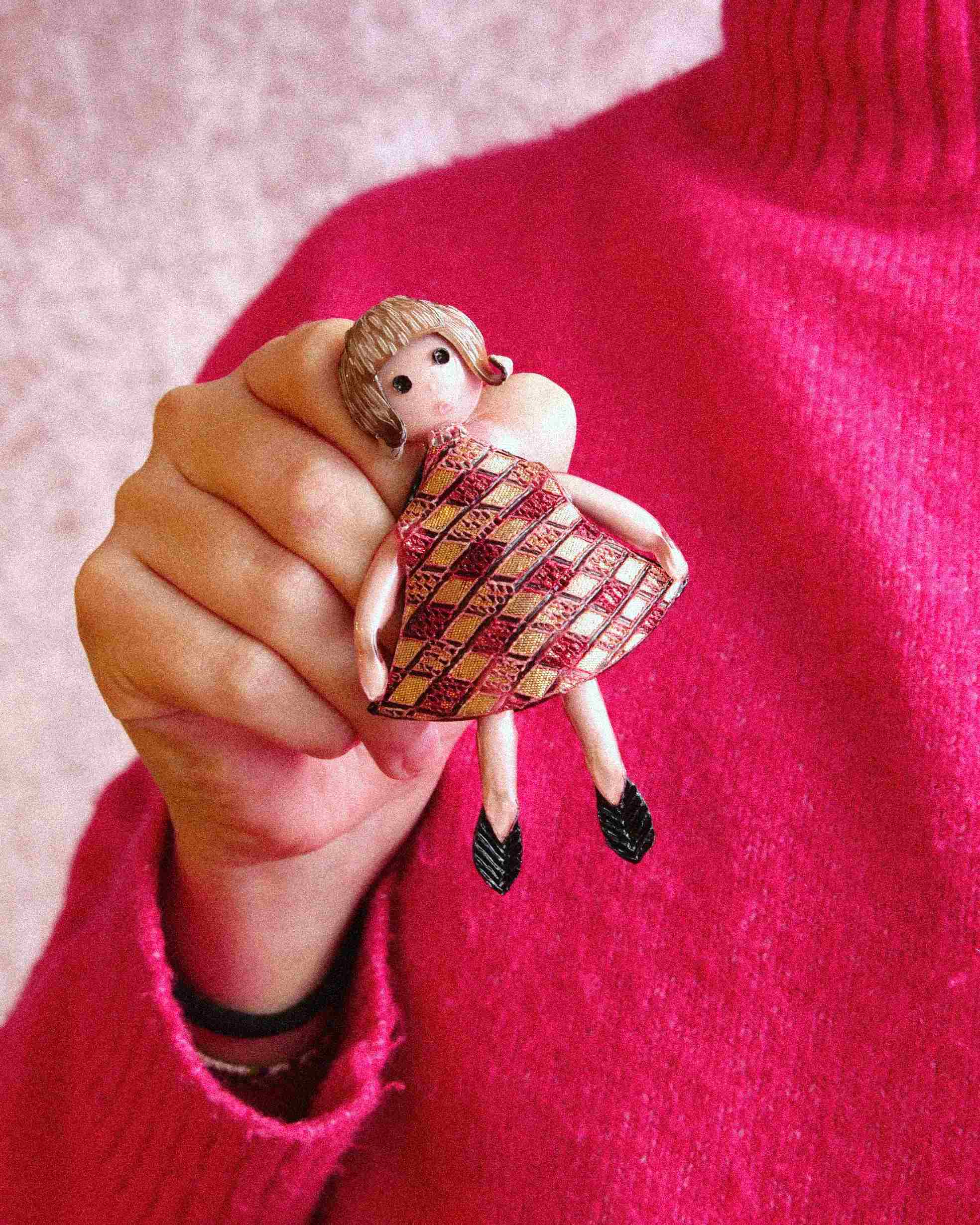 Femme avec un col roulé rose fuchsia montrant une broche en forme de personnage féminin avec robe rouge