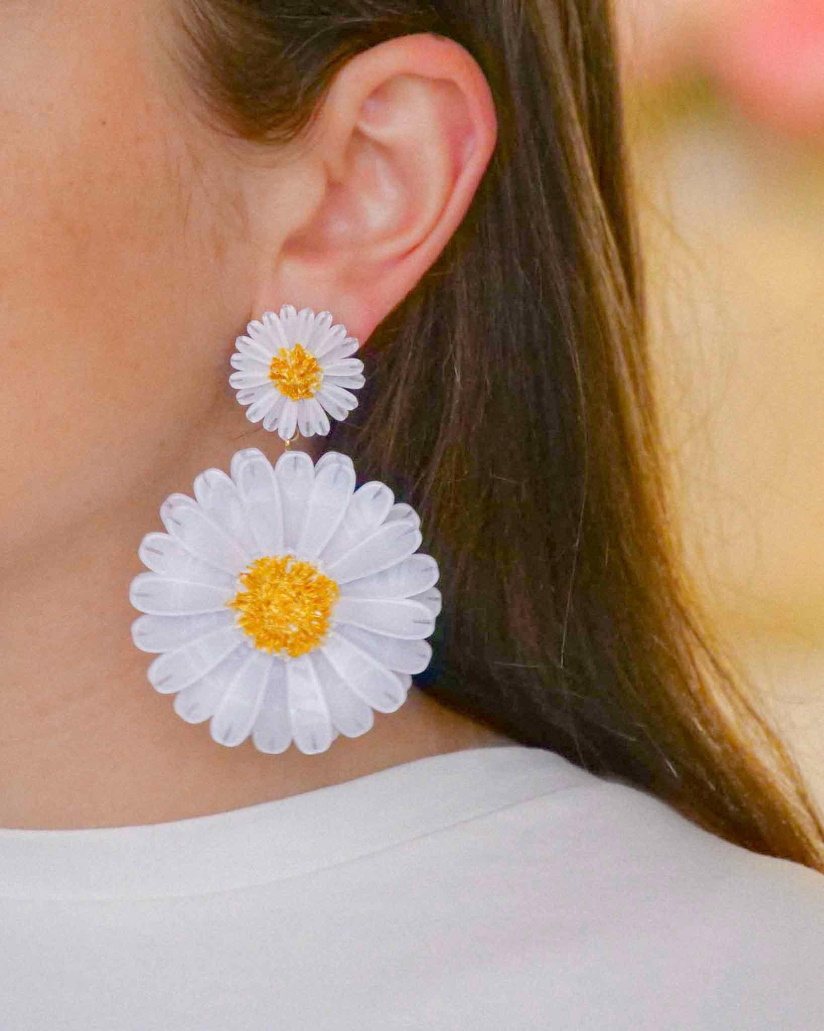 Oreille de femme brune portant une boucle d'oreilles pendantes marguerites avec deux fleurs