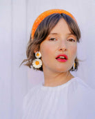 Femme avec serre tête orange a strass portant des boucles d'oreilles marguerites blanches