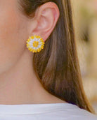 all-groups Femme brune portant des petites boucles d'oreilles puces marguerites blanches aux bords jaune