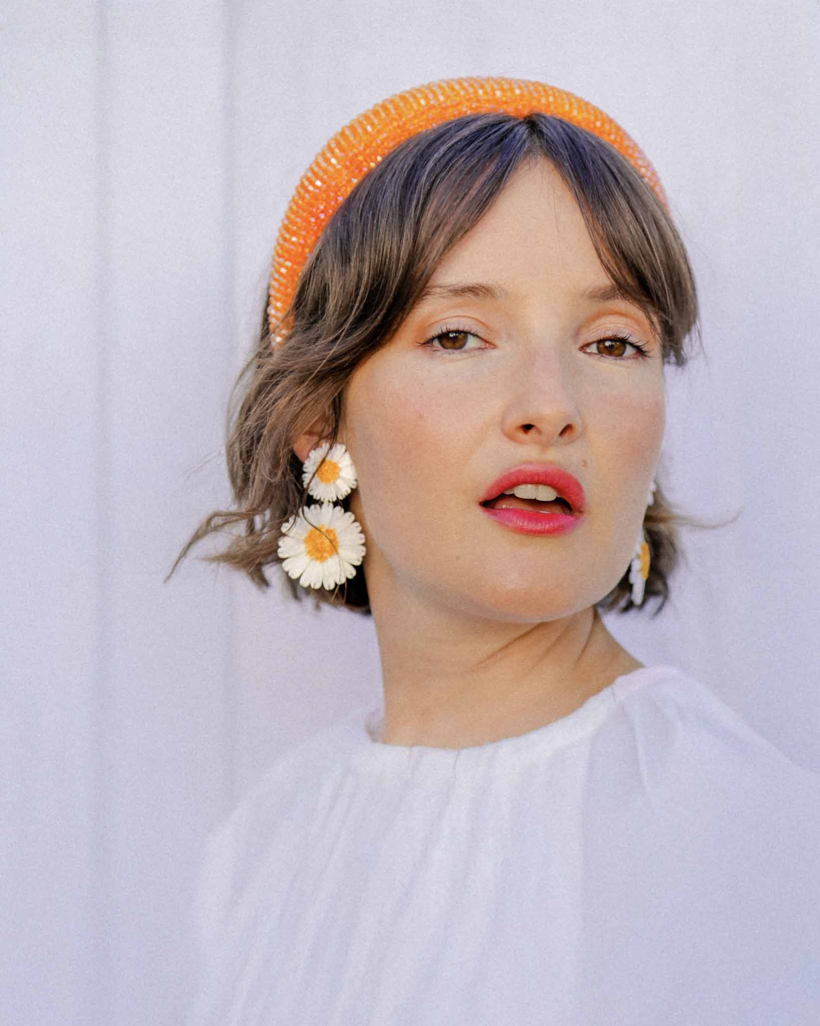 Boucles d'oreilles fleuries portées sur une femme aux cheveux courts avec un bandeau orange 