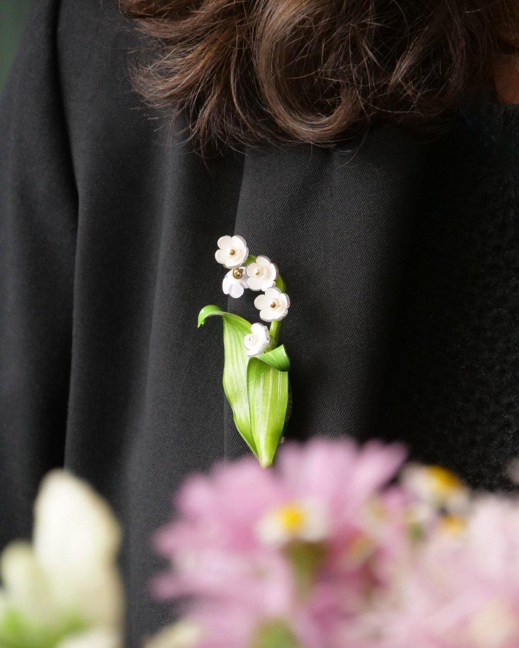 all-groups Femme portant une veste costume noire sur laquelle est accrochée une broche muguet