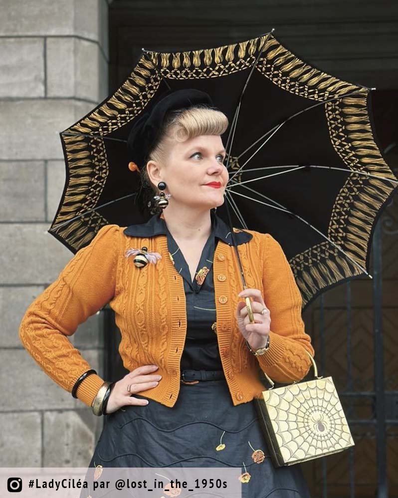 femme avec parapluie et gilet orange qui porte des boucles d'oreilles et une broche bijou