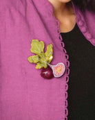 all-groups Femme portant une broche figue violette et verte sur une veste de costume rose