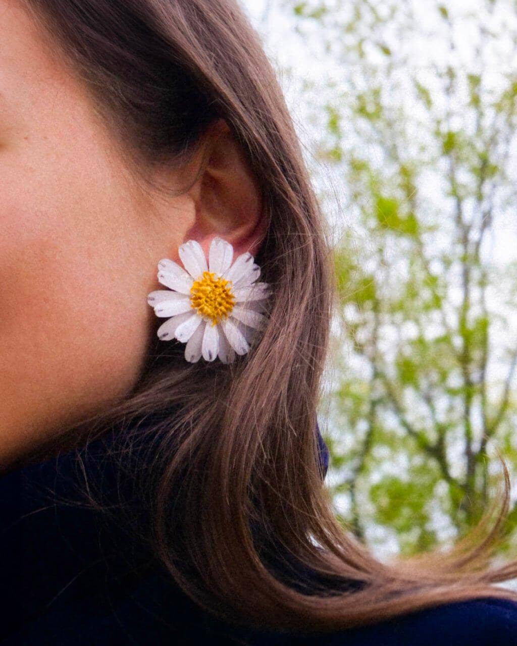 all-groups Femme brune dans un parc portant un col roulé et des boucles d'oreilles marguerites blanches réalistes