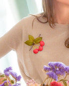 Broche cerises rouges portée sur un pull