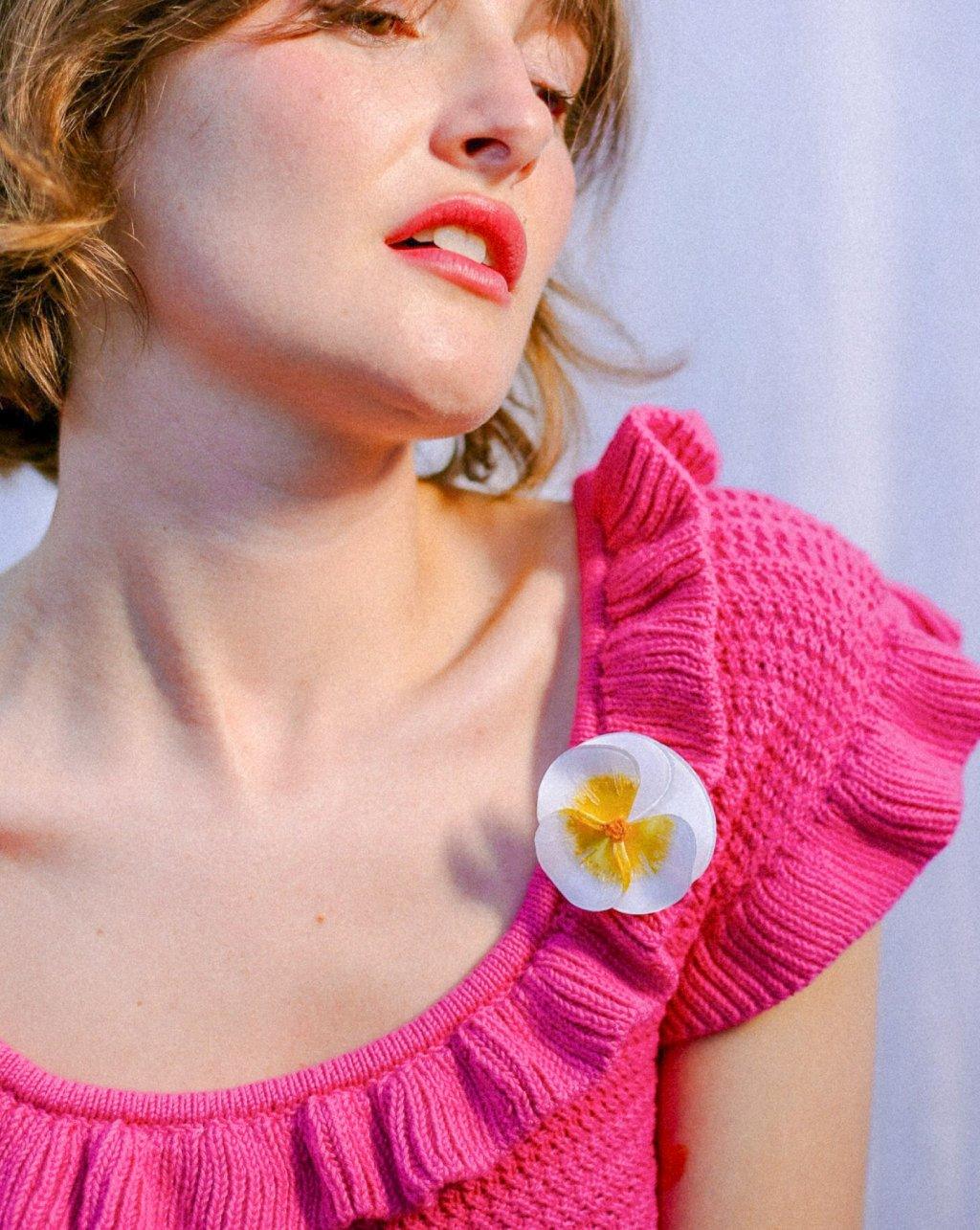 all-groups Femme blanche brune portant un pull rose fuchsia avec une broche blanche et dorée fleur